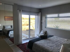 A bedroom with a bed, a chair, a desk, and a sliding glass door leading to an outdoor area.