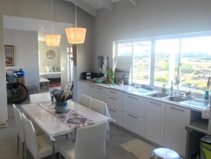A modern kitchen with white cabinets, a dining table, pendant lights, and a view of the countryside.