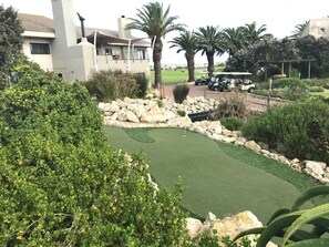 A golf course with a putting green, palm trees, and a building in the background.