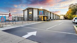 L’entrée d’un hôtel de luxe, classé six étoiles, avec une allée bordée de portails, un parking et un SUV blanc garé à proximité.