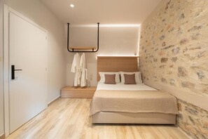 A bedroom with a bed, a wooden headboard, a stone wall, and a white door. - Nest in the City Apartment Home to Home Mgmt (Volos)