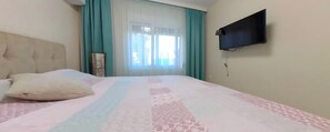 Un dormitorio con una cama, un televisor montado en la pared y un ventanal con cortinas.