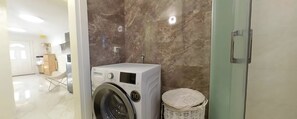 Een moderne wasruimte met een voorlader wasmachine, een betegelde muur van marmer en een rieten mand.
