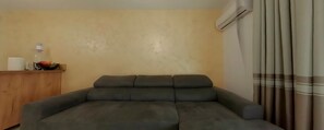 Una sala de estar con un sofá gris oscuro, un mueble de madera, un equipo de aire acondicionado y una cortina.