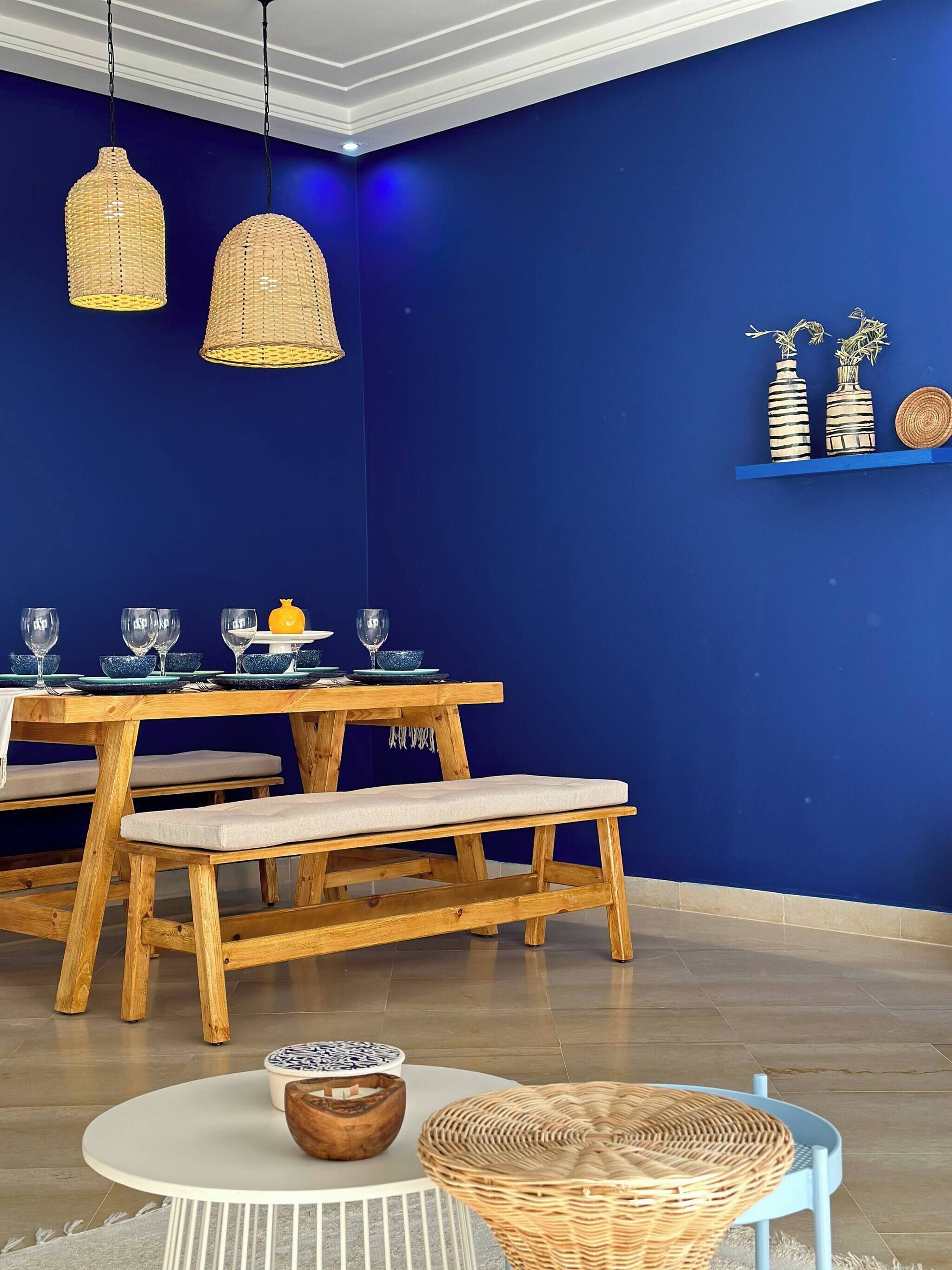 A dining area with a wooden table and bench, blue walls, hanging wicker lamps, and decorative items on a shelf.
