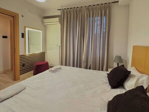 Ein Hotelzimmer mit einem Bett, einem roten Hocker, einer Lampe, einem Vorhangfenster und einer Heizung.