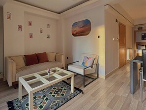 A living room with a sofa, a chair, a coffee table, a rug, and a painting on the wall. - Taksim Square—1BR Suite 04 (Beyoğlu)