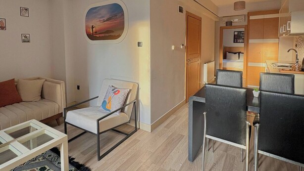 Un salon moderne avec un canapé, un fauteuil, une table basse en verre et une vue sur la cuisine.