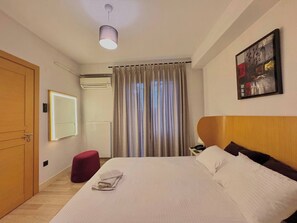 A hotel room with a bed, a red ottoman, a wall-mounted mirror, an air conditioning unit, a ceiling light, and a painting on the wall. - Taksim Square—1BR Suite 04 (Beyoğlu)