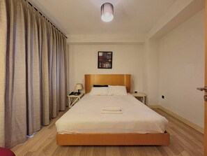 A hotel room with a single bed, a bedside table with a lamp, a wall-mounted artwork, and a door on the right. - Taksim Square—1BR Suite 04 (Beyoğlu)