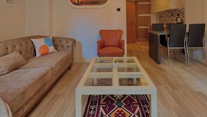 Una sala de estar con sofá, sillón, una mesa de centro de vidrio y un cuadro en la pared.