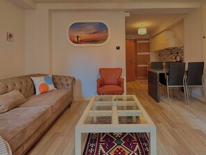Ein Wohnzimmer mit einer Couch, einem Sessel, einem Glastisch und einem Gemälde an der Wand.