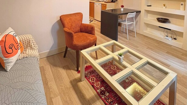A modern living room with a sofa, armchair, glass coffee table, and a painting on the wall. - Taksim Square—1BR Suite 01 (Beyoğlu)