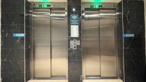 Deux portes d’ascenseur équipées d’écrans numériques, un panneau indiquant une zone accessible aux personnes handicapées et un panneau « interdiction de fumer ».