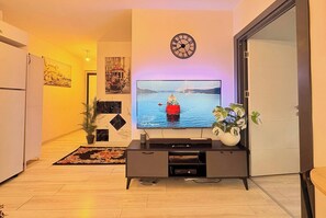 A living room with a flat-screen TV, a clock, a potted plant, and a decorative rug. - Bright & Modern 2BR Apartment in Kağıthane (Kağıthane)