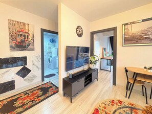 A modern living room with a flat-screen TV, a dining area with a table and chairs, and a hallway leading to a bathroom. - Bright & Modern 2BR Apartment in Kağıthane (Kağıthane)