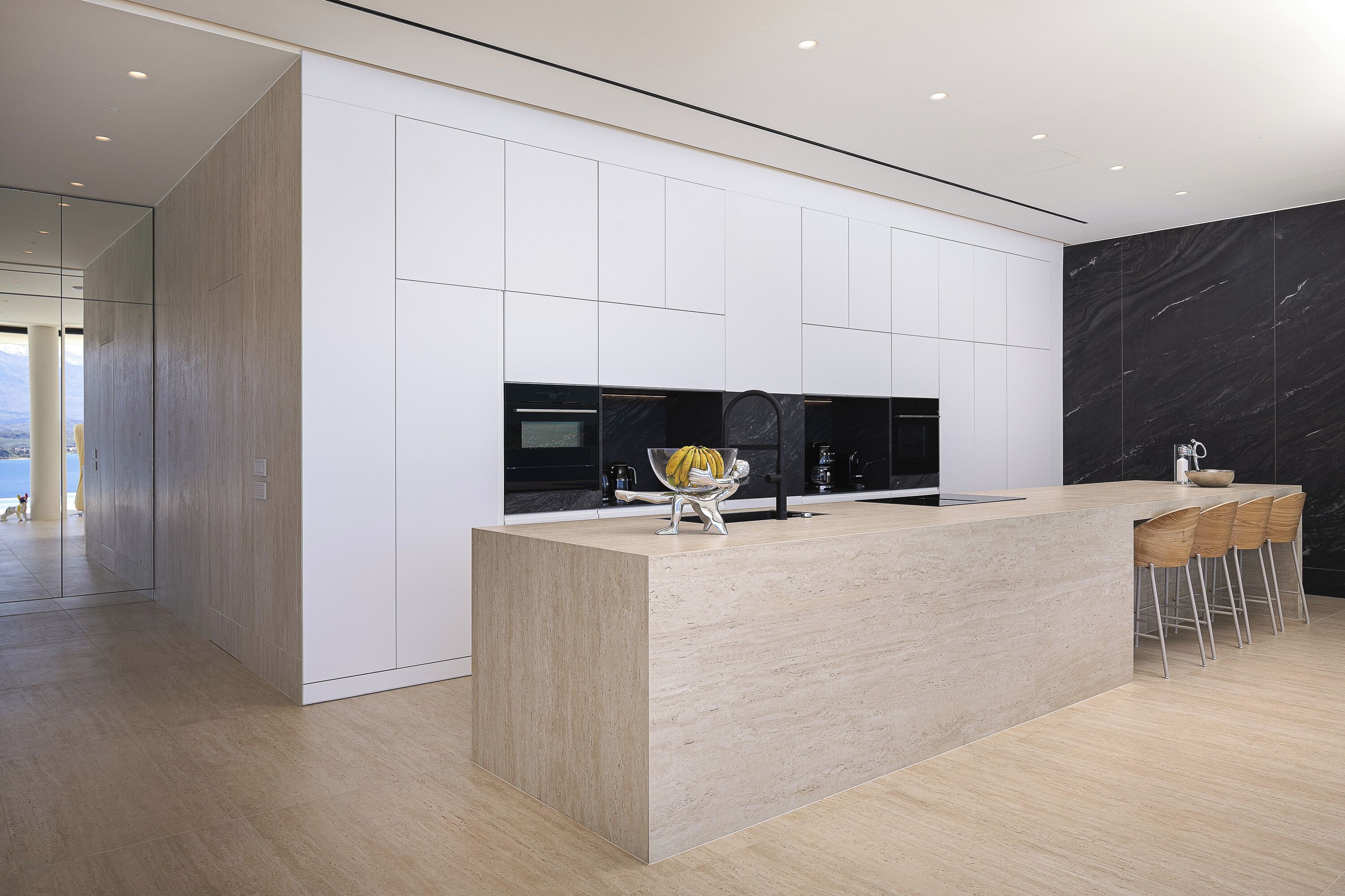 A modern kitchen with a central island, bar stools, and a view of the outdoors.