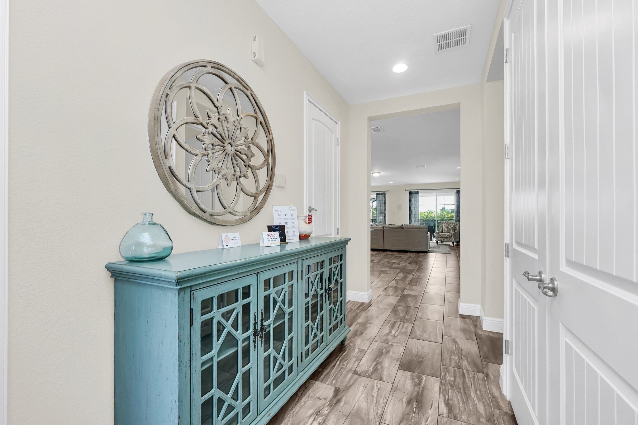 A hallway with a light blue console table, a decorative wall piece, and a door leading to a living area.