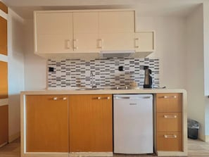 A compact kitchen with wooden cabinets, a white dishwasher, and a tiled backsplash. - Taksim Square—1 Bedroom Suite 05 (Beyoğlu)