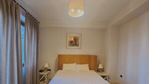 Ein Hotelzimmer mit einem gro ßen Bett, zwei Nachttischen mit Lampen, einem Gemälde an der Wand und einem Fenster mit Vorhängen.