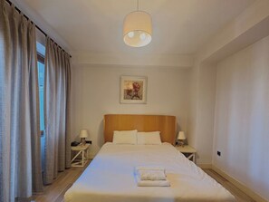 A hotel room with a large bed, two bedside tables with lamps, a painting on the wall, and a window with curtains. - Taksim Square—1 Bedroom Suite 05 (Beyoğlu)