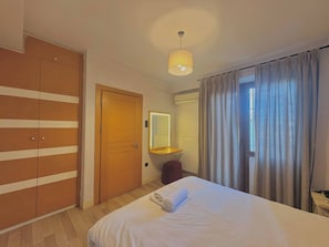 A hotel room with a bed, a wardrobe, a mirror, a bedside table, and a window with curtains. - Taksim Square—1 Bedroom Suite 05 (Beyoğlu)
