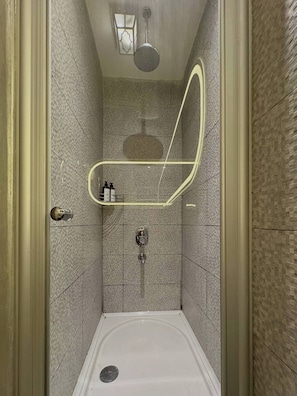 A small, tiled shower stall with a handheld showerhead, a wall-mounted faucet, and a light fixture above. - Taksim Square—1 Bedroom Suite 05 (Beyoğlu)