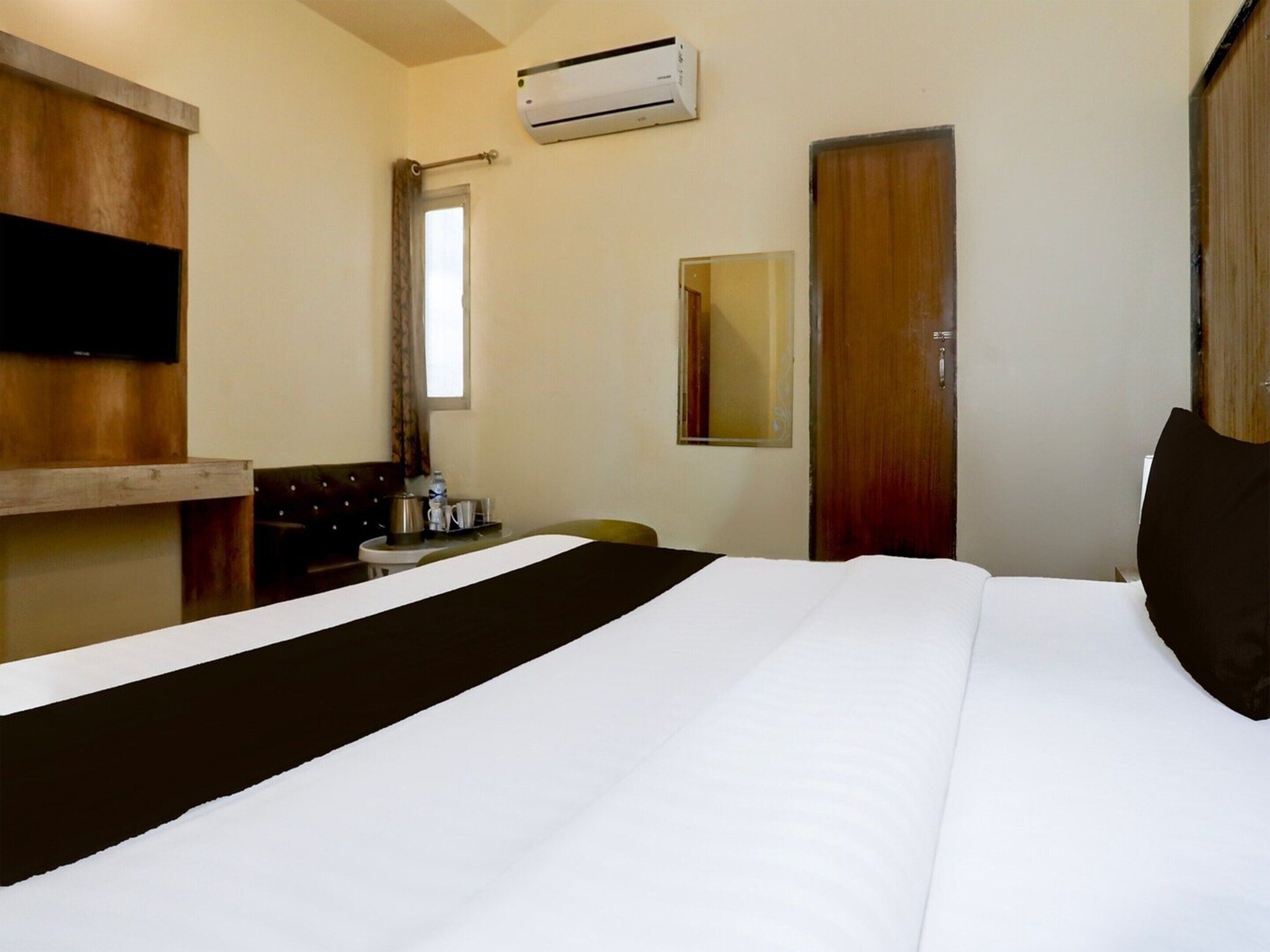 A hotel room with a bed, a flat-screen TV, an air conditioning unit, a window, and a door.