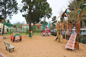 Ein Spielplatz mit Sand, einer Bank und einer Kletterkonstruktion.