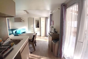 Eine kompakte Küche mit Spüle, ein Essbereich mit Stühlen und Blick durch ein Fenster mit gemusterten Vorhängen.