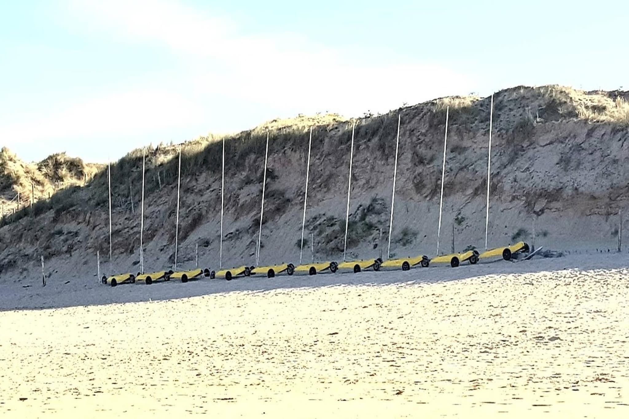 En sandstrand med en rad gula bilar som står parkerade på led.