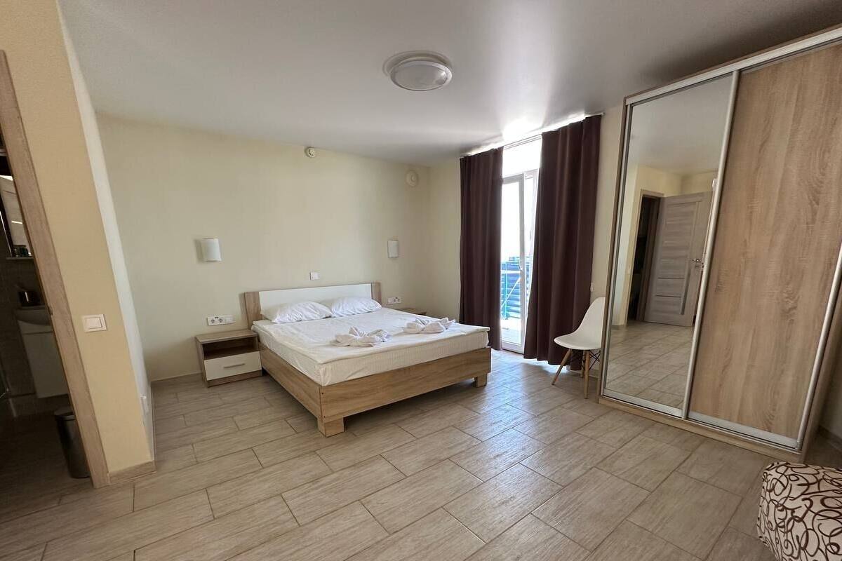 A hotel room with a bed, a wardrobe, a mirror, a bedside table, and a view of the outside.