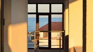 Un pasillo con vistas al mar a través de amplios ventanales, barandilla de metal y suelo de baldosas.