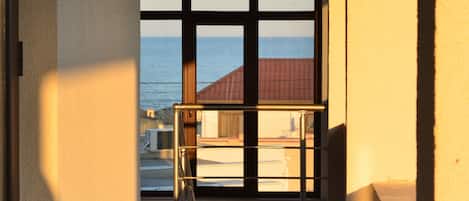 A corridor with a view of the sea through large windows, a metal railing, and a tiled floor.