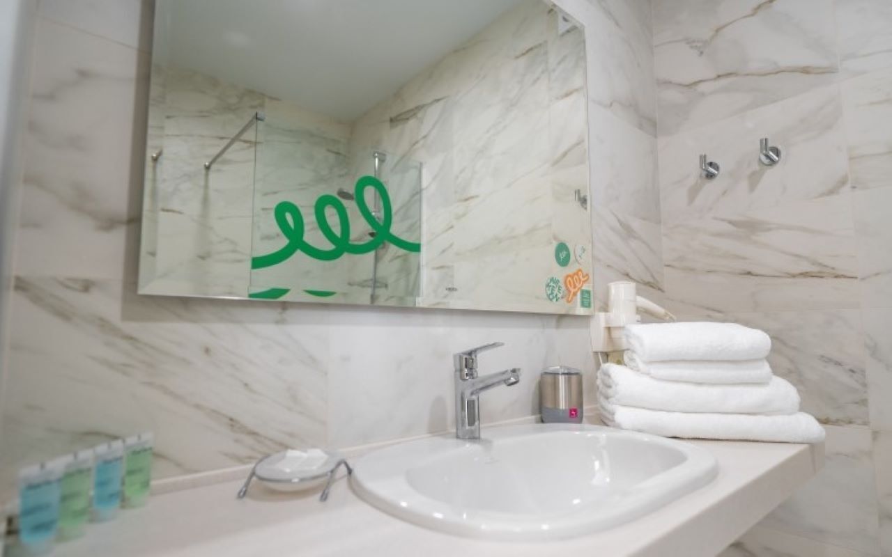 Une salle de bain avec un mur en marbre, un lavabo avec un miroir et un porte-serviettes.