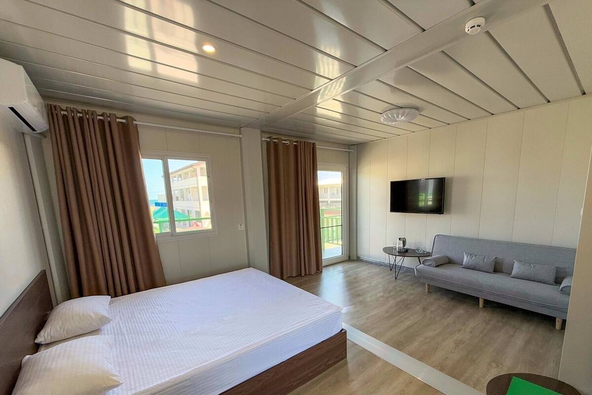 A hotel room with a bed, a sofa, a TV, and a balcony with curtains.