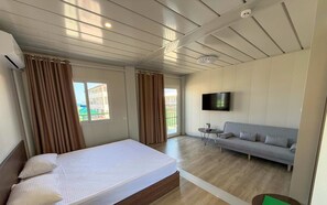 Habitación de hotel con cama, sofá, televisión y balcón con cortinas.