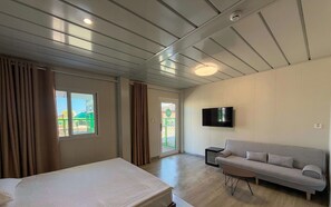 Una habitación con cama, sofá, televisión y ventana con cortinas.