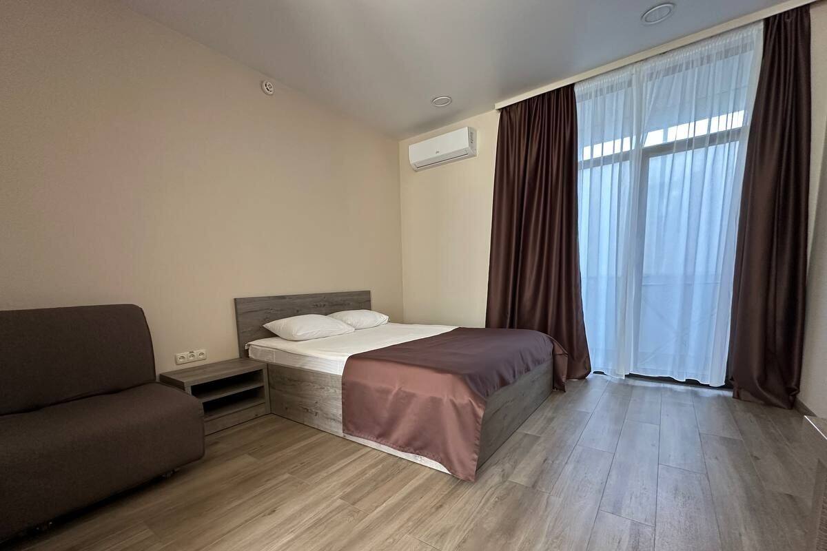 A bedroom with a bed, a sofa, a bedside table, and a window with curtains.