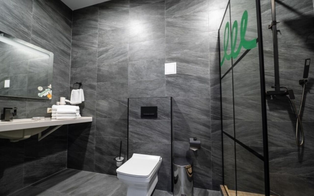 A modern bathroom with a dark marble wall, a white toilet, a sink with a towel rack, and a glass shower enclosure.