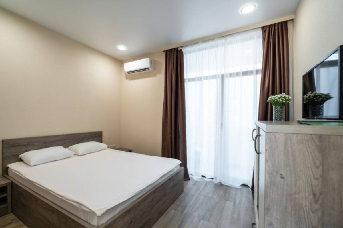 A bedroom with a bed, a nightstand, a TV, and a window with curtains.