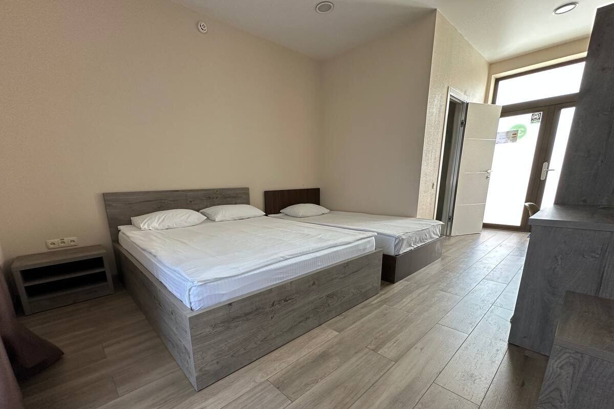 A bedroom with two beds, a wooden floor, a small shelf, and a door leading to another room.