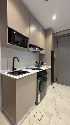 A compact kitchen with a built-in microwave, a sink, a coffee maker, and a washing machine. - 310 tara-JRE Jabal Al Lweibdeh with stunning view (Amman)