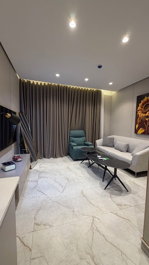 Ein modernes Wohnzimmer mit einer Couch, einem grünen Sessel, einem Couchtisch, einem Fernseher und einem Bild an der Wand.