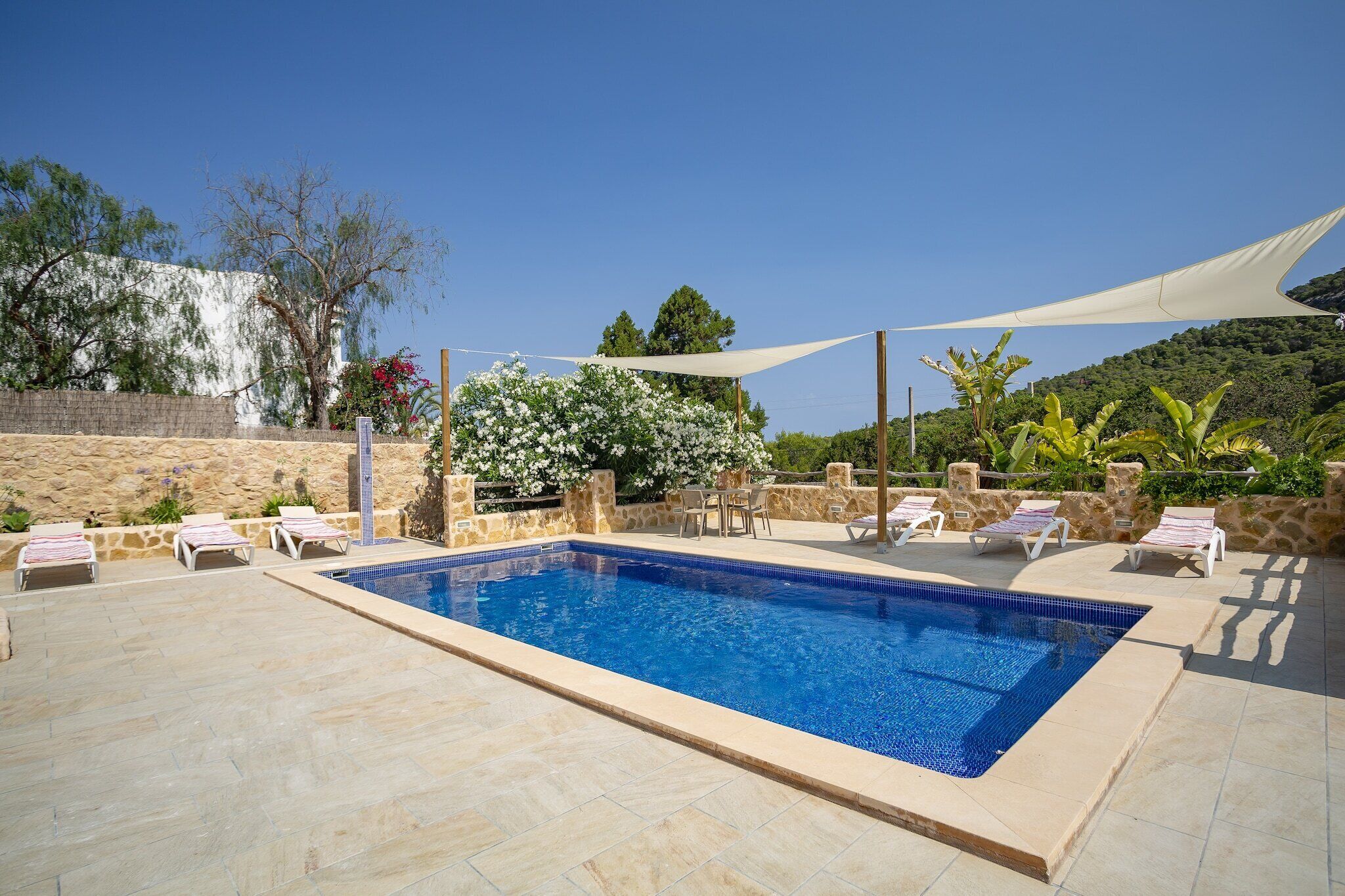 Une piscine rectangulaire bordée de carreaux, entourée de murs en pierre et surmontée d’un auvent blanc.