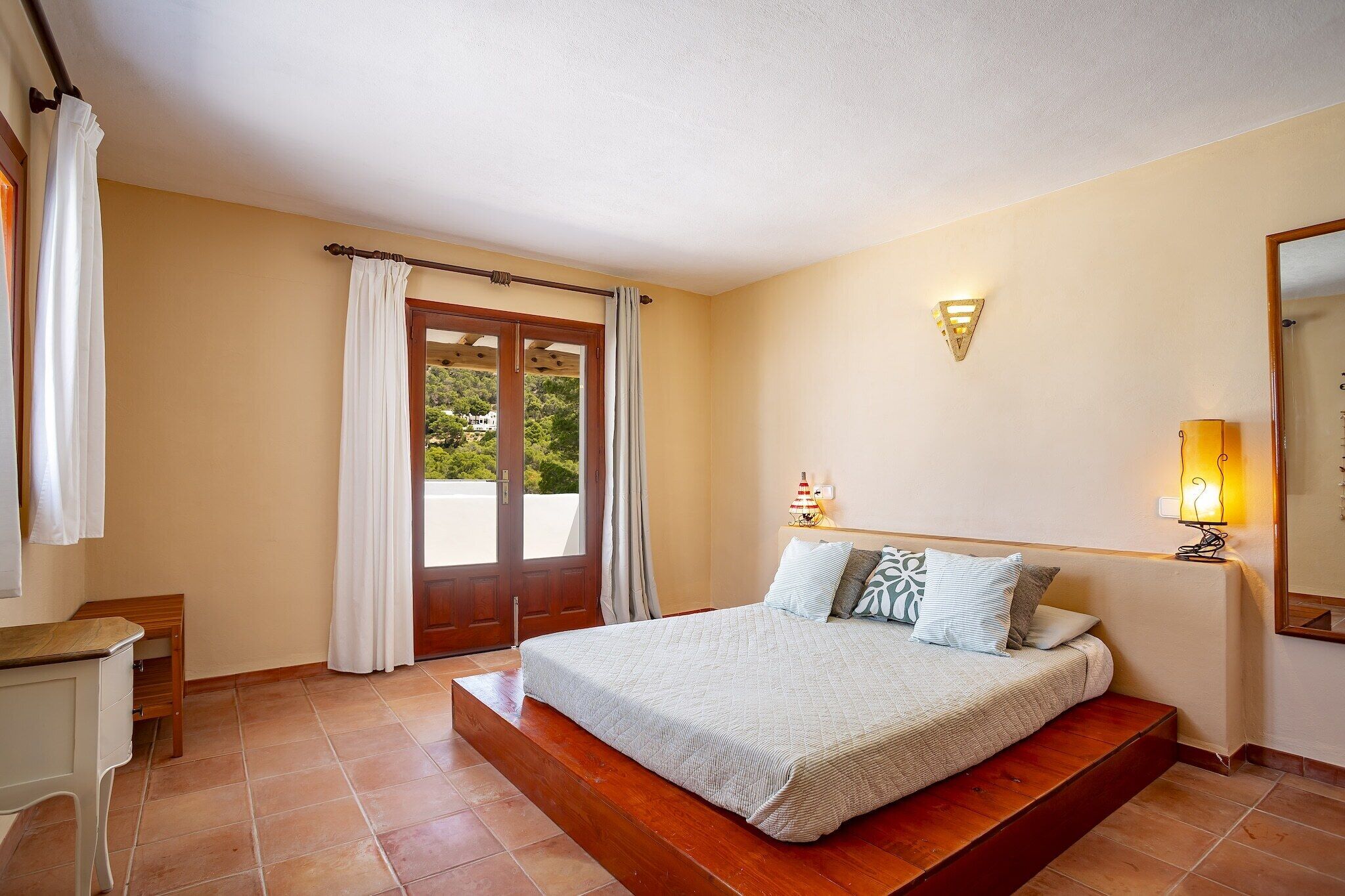 Une chambre à coucher comprenant un lit, un bureau, une chaise, une fenêtre avec des rideaux et un luminaire fixé au mur.