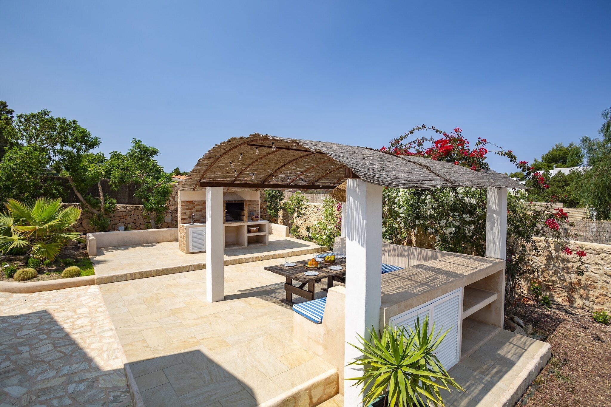 Un espacio de estar al aire libre cubierto con una mesa, sillas, una pérgola y un muro de piedra con plantas.