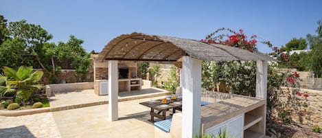 Un espacio de estar al aire libre cubierto con una mesa, sillas, una pérgola y un muro de piedra con plantas.