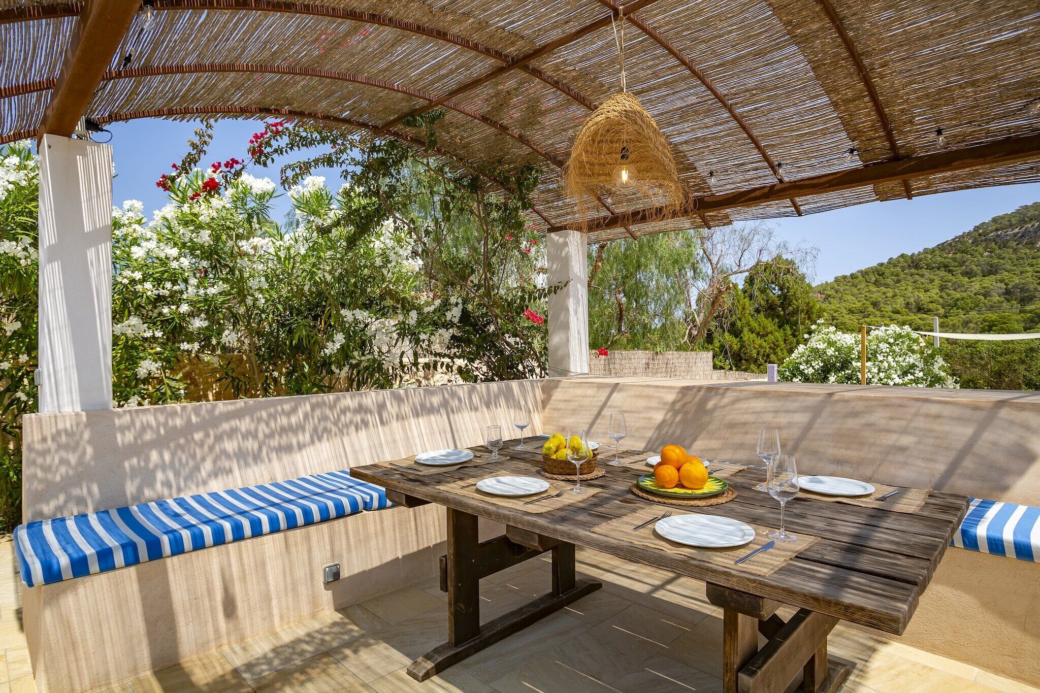 Un área de comedor al aire libre con una mesa dispuesta para cuatro personas, rodeada de bancos acolchados.