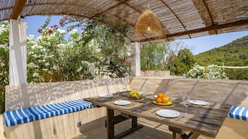 An outdoor dining area with a table set for four, surrounded by cushioned benches.
